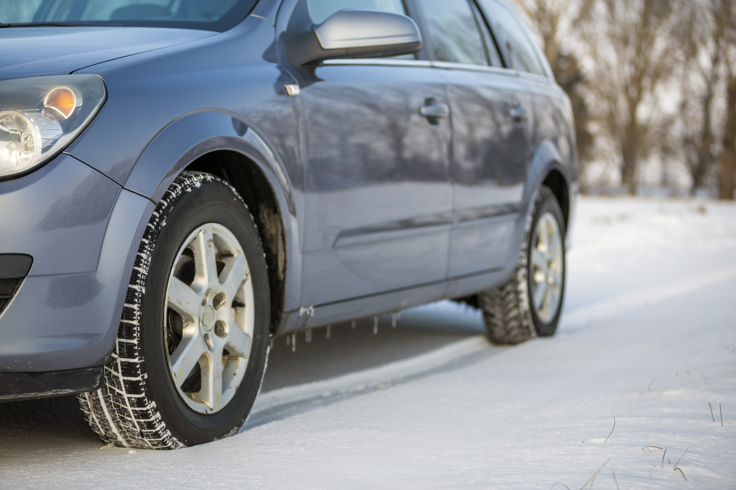 Close up of a car tire parked on snowy road on winter day. Transportation and safety concept.